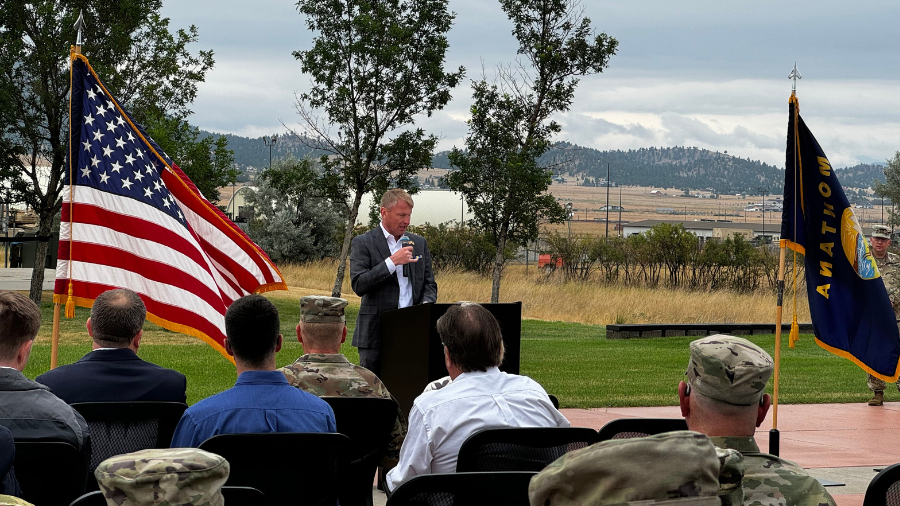 Man speaks from podium beside American flag. 